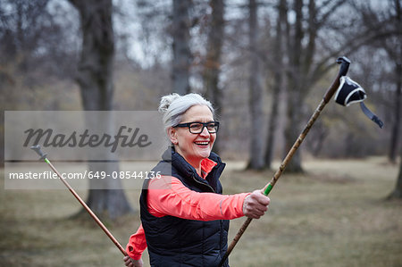 Mature female training in park, exercising with nordic walking poles