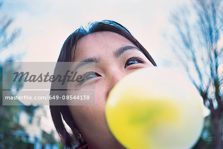 Close up of young woman blowing yellow bubble gum bubble