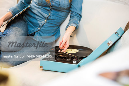 Cropped shot of young woman sitting on sofa listening to vintage record player