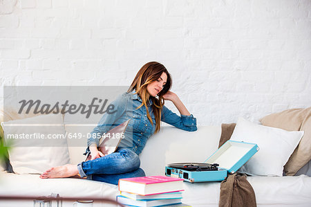 Young woman sitting on sofa listening to music on vintage record player