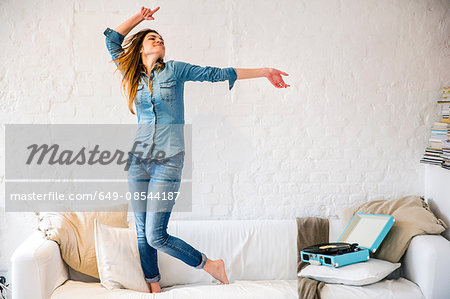 Young woman standing on sofa dancing to vintage record player