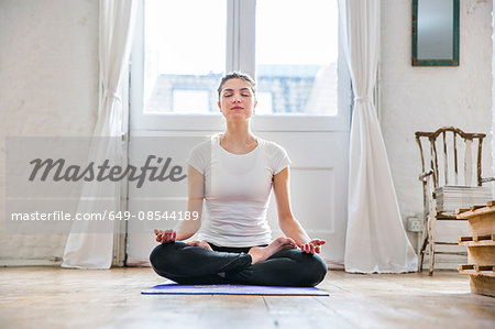 Young woman practicing yoga lotus position in apartment