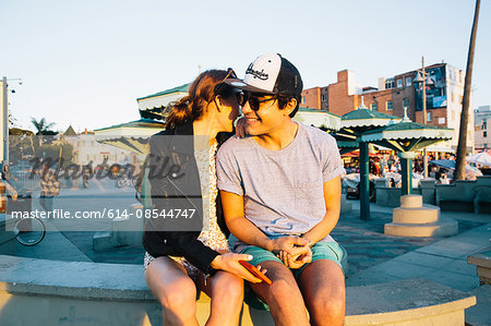 Romantic young couple sitting on wall at coast, Venice Beach, California, USA