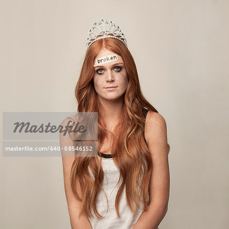 Studio portrait of redhead woman with tiara and broken sign on forehead