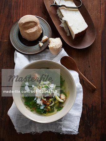 Overhead view of italian wedding soup with bread roll and parmesan cheese