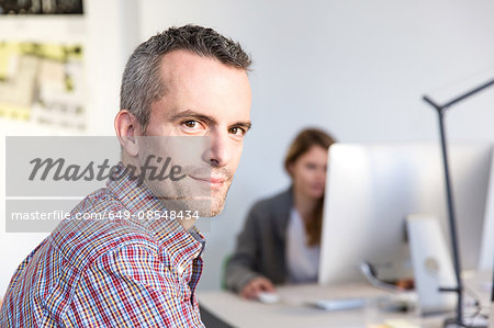 Side view of mature man in office looking at camera smiling