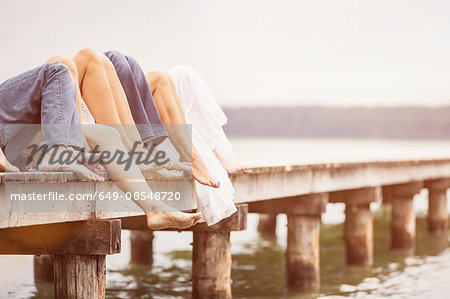 Group of friends relaxing on pier, focus on feet