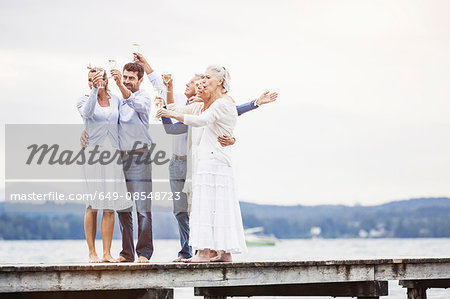 Group of friends standing on pier, holding wine glasses, making a toast