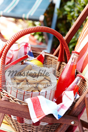 Cantucci biscuits in biscuit tin with glass bottles of juice in picnic basket
