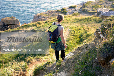 High angle rear view of hiker with backpack hiking down cliff side, Portland, UK