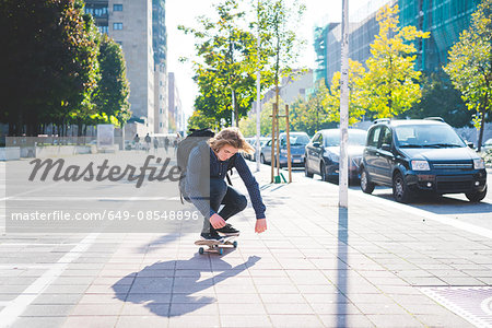 Young male skateboarder crouching whilst skateboarding on sidewalk