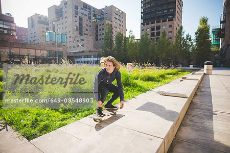 Young male skateboarder crouching whilst skateboarding on urban wall