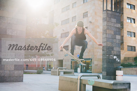 Young male skateboarder jumping over urban concourse seat