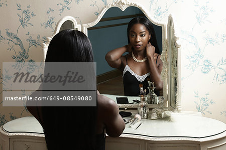 Young woman sitting at dressing table, putting on necklace Young woman sitting at dressing table, putting on necklace