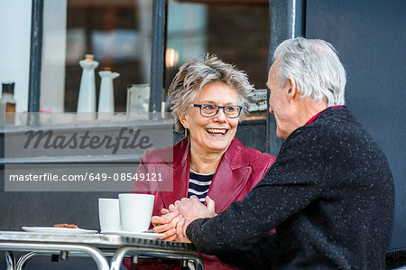 Romantic senior couple holding hands at sidewalk cafe