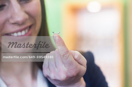 Woman holding contact lens on finger smiling