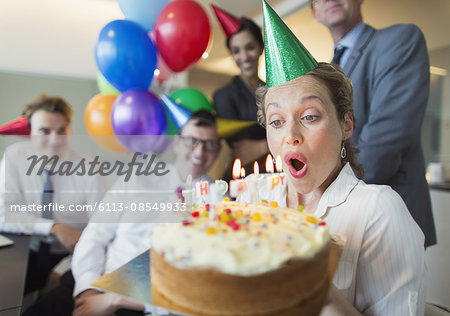 Colleagues watching businesswoman blowing out birthday cake candles