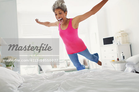 Playful mature woman jumping onto bed