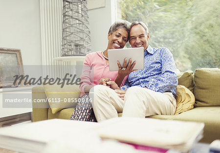 Smiling mature couple using digital tablet on living room sofa