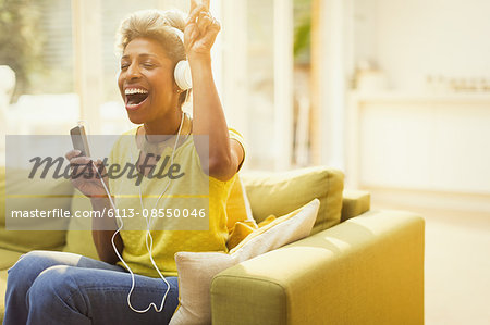 Playful mature woman listening to headphones with MP3 player in living room