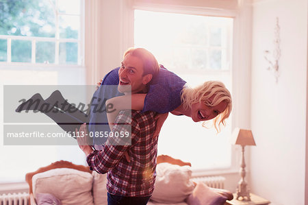 Portrait playful husband carrying wife over shoulder in living room