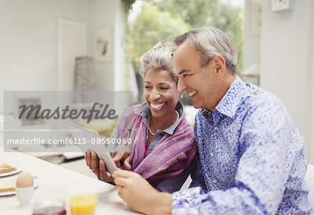 Smiling mature couple sharing digital tablet at breakfast table Smiling mature couple sharing digital tablet at breakfast table