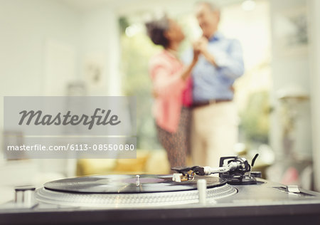 Mature couple dancing in living room behind record player Mature couple dancing in living room behind record player