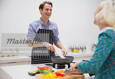 Smiling couple cutting and cooking vegetables in kitchen