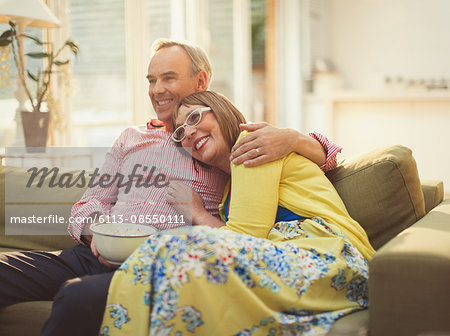 Affectionate mature couple watching TV and eating popcorn on living room sofa