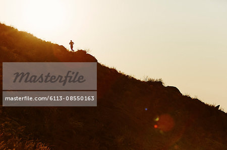 Silhouette of runner ascending hillside at sunset