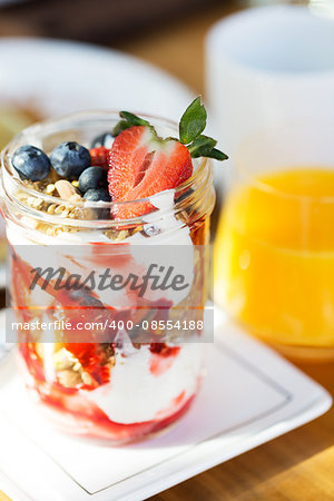 close-up of glass jar filled with homemade granola, yogurt and fresh berries served for breakfast with orange juice, healthy eating and lifestyle concept