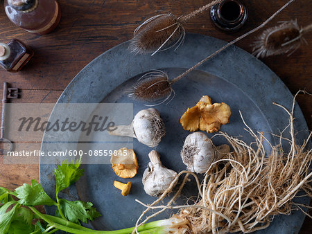 Overhead View of Pewter Plate with Wild Mushrooms, Garlic and Celery on Wooden Surface with Old Key, Bottles and Dried Bullrushes