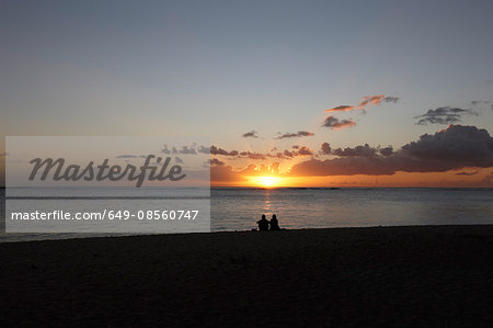 Couple sitting on beach at sunset