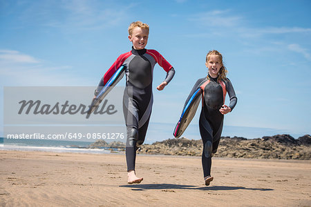 Children in wetsuits carrying surfboards