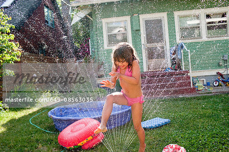 Young girl playing in garden sprinkler
