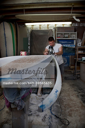 Mature man sawing a surfboard in his workshop