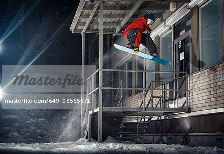 Mid adult male snowboarder jumping mid air from building at night