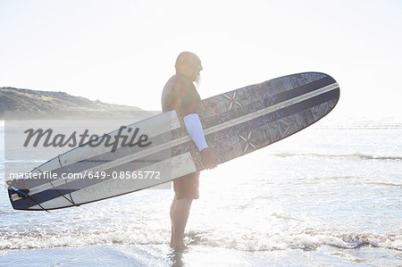 Mature male surfer watching sea from beach