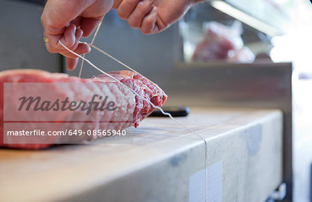 Close up of butchers hands tying meat joint on butchers block