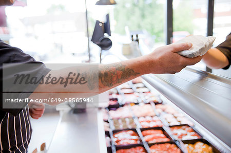 Cropped shot of butcher handing produce to customer in butchers shop