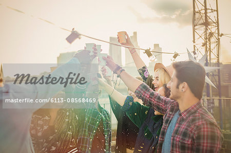 Enthusiastic young adults toasting cocktails at rooftop party