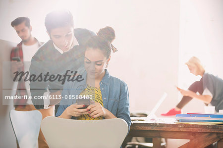 Young man and woman texting with cell phone in office