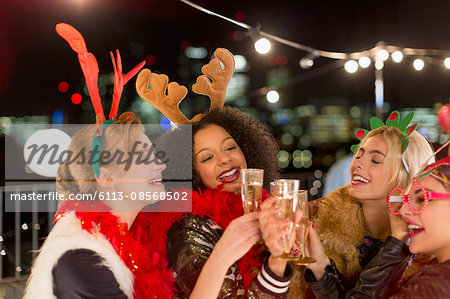 Young women wearing Christmas reindeer antlers and toasting champagne glasses at rooftop party