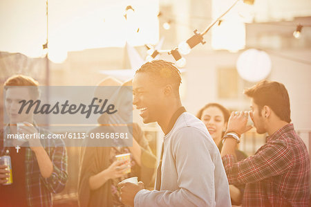 Young man laughing and drinking at rooftop party