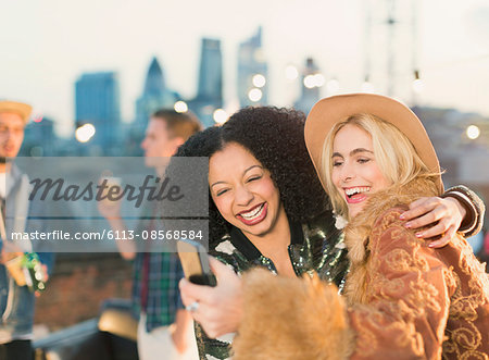 Laughing young women taking selfie at rooftop party