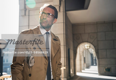 Corporate businessman in trench coat standing in sunny cloister