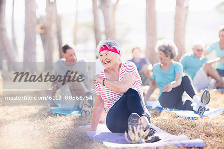 Smiling senior woman practicing yoga in sunny park