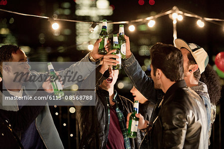 Young men toasting beer bottles at rooftop party