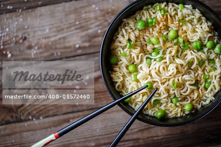 Top view of chinese noodles with fresh peas and chopped green onion on wooden table.