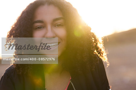 Beautiful happy mixed race African American girl teenager female young woman with perfect teeth smiling in golden light with sun flare at sunset or sunrise